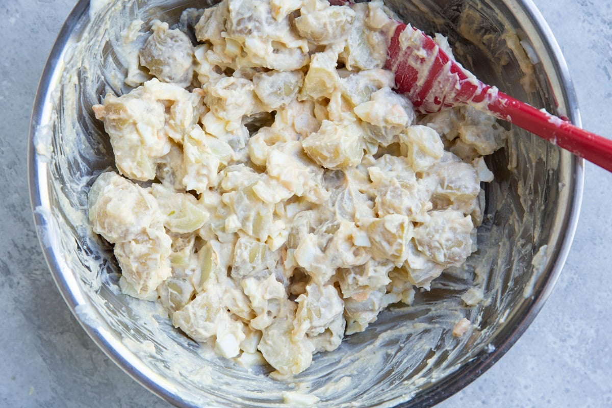 Stainless steel bowl of cottage cheese potato salad all mixed up with a red rubber spatula.
