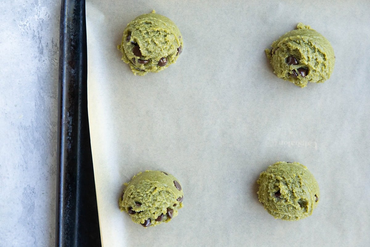 Cookie sheet lined in parchment paper with mounds of pistachio cookie dough on top.