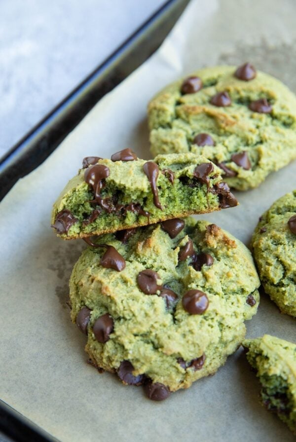 Pistachio cookies on a baking sheet with one of them sliced in half to expose the gooey center.