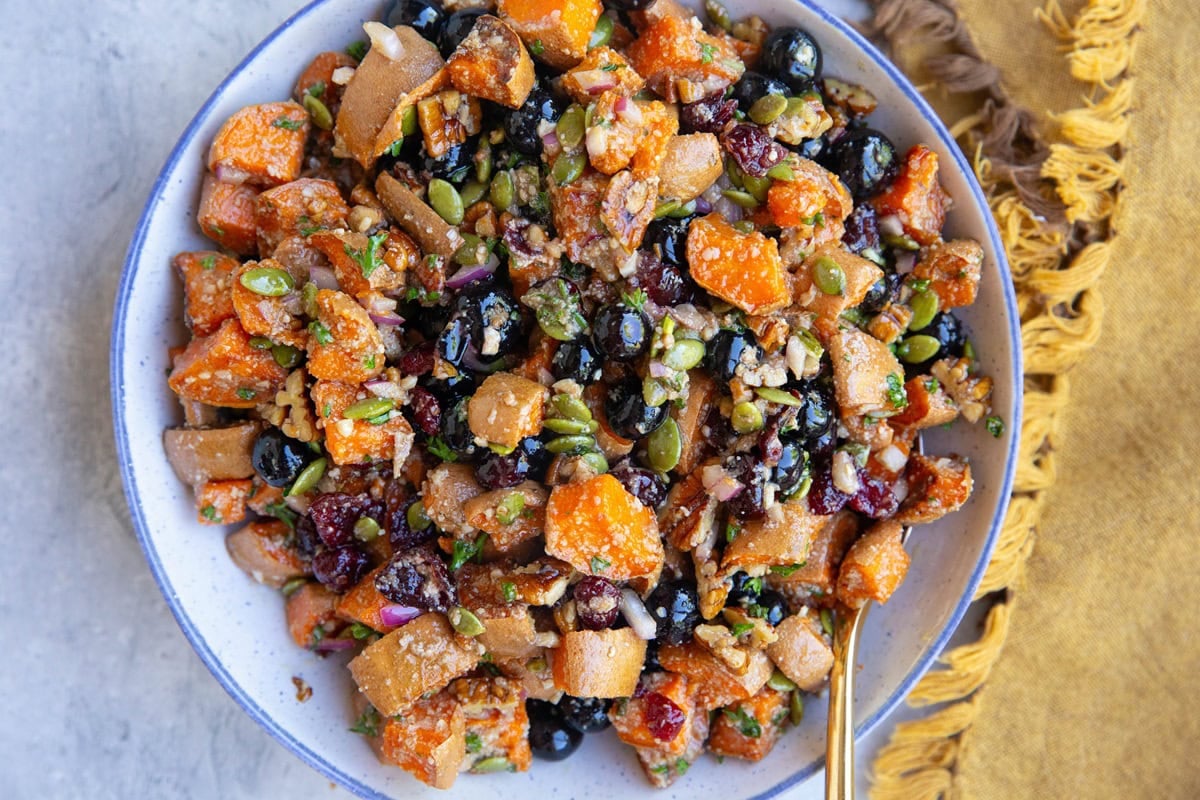 Bowl full of sweet potato salad with a golden spoon and a golden napkin to the side, ready to serve.
