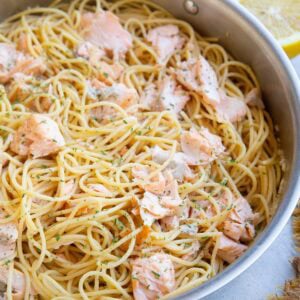 Stainless steel skillet full of salmon pasta with a lemon sliced in half in the background.