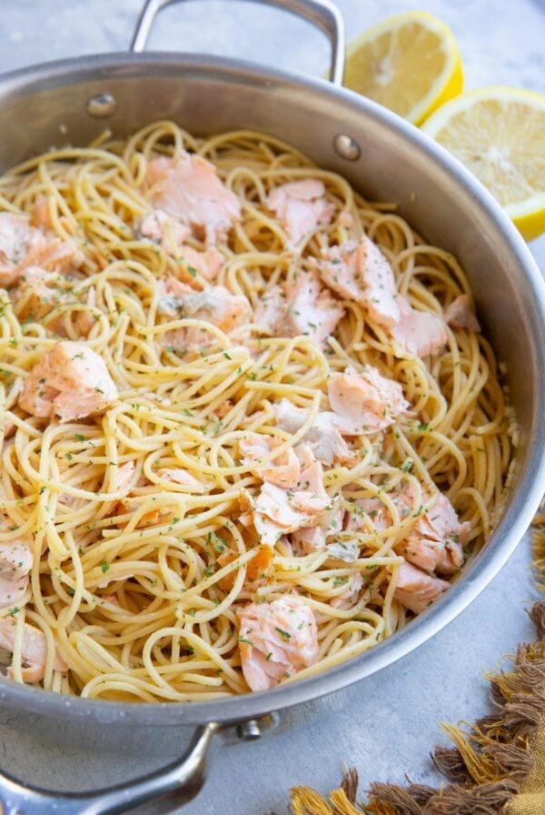 Stainless steel skillet full of salmon pasta with a lemon sliced in half in the background.