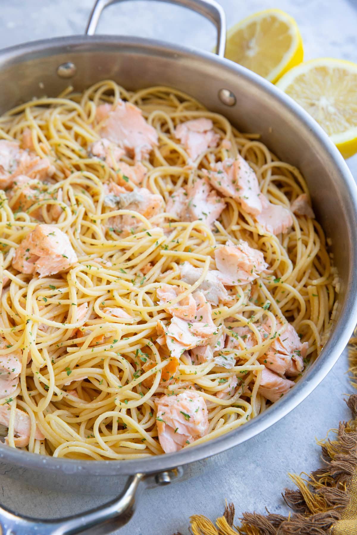 Stainless steel skillet full of salmon pasta with a lemon sliced in half in the background.