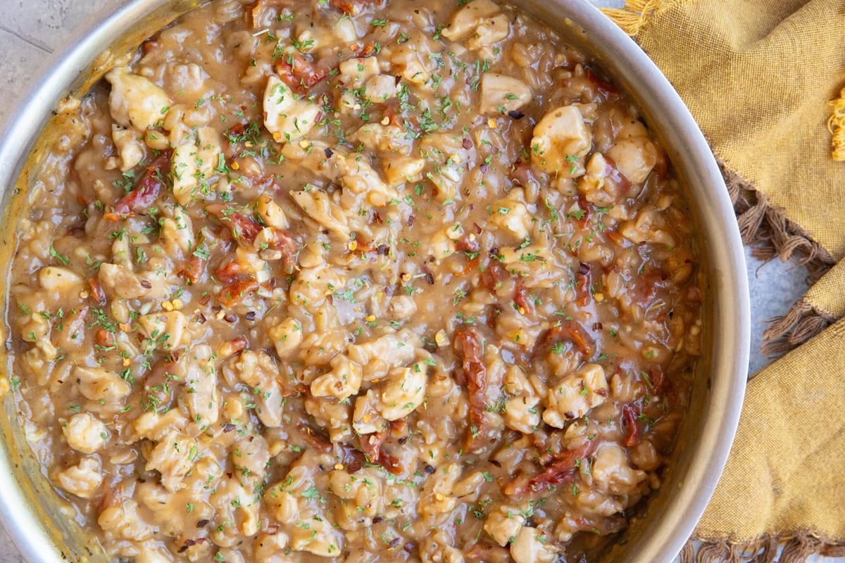 Stainless steel skillet full of chicken orzo with a golden napkin to the side.