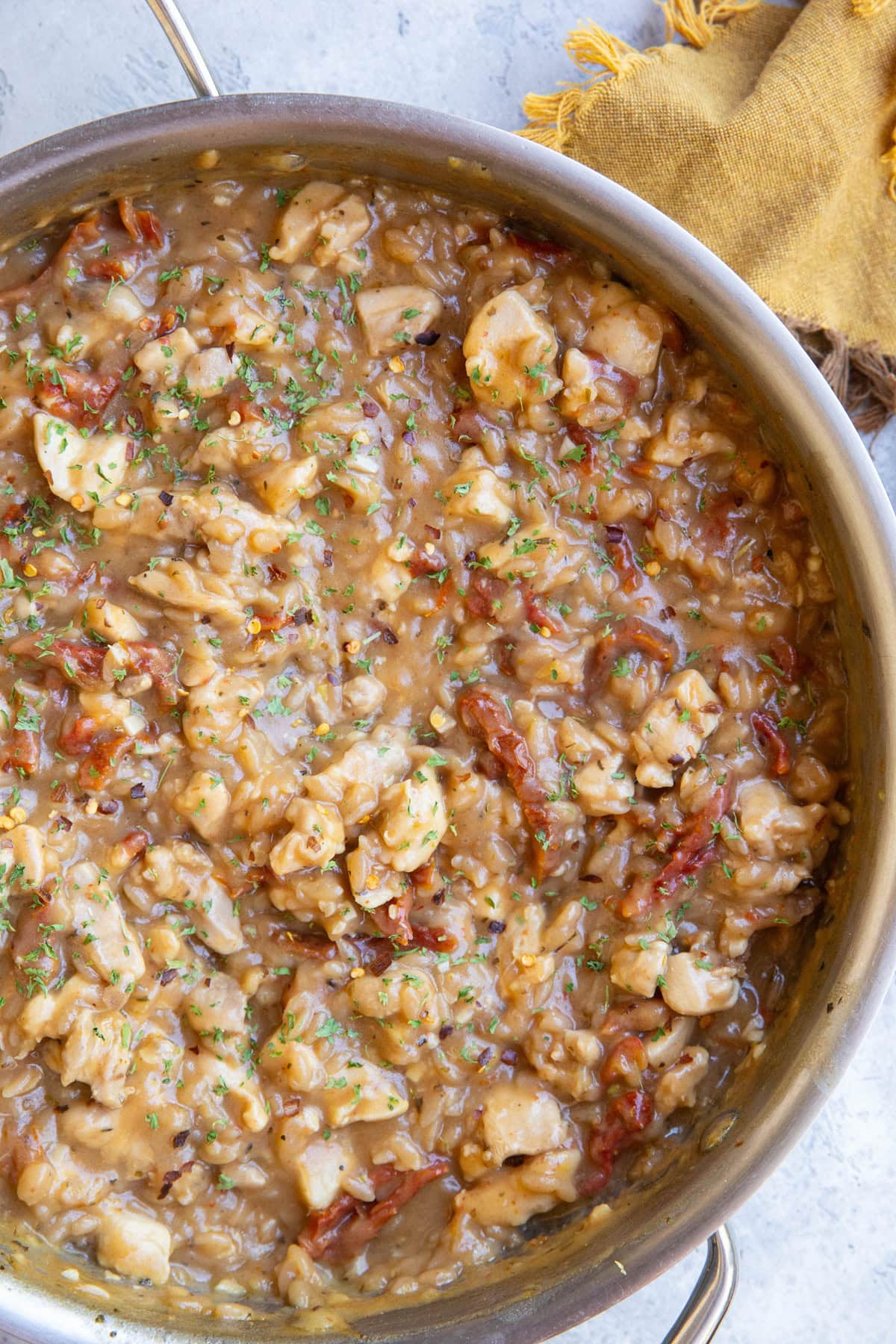 Stainless steel skillet full of sun-dried tomato chicken orzo sprinkled with dried parsley and ready to serve.