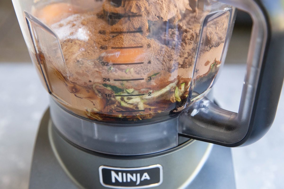 Food processor with ingredients for zucchini chocolate cake.