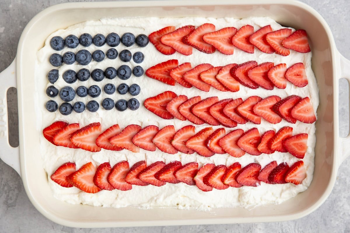 Flag cake in a large casserole dish with white frosting, blueberries, and strawberries.