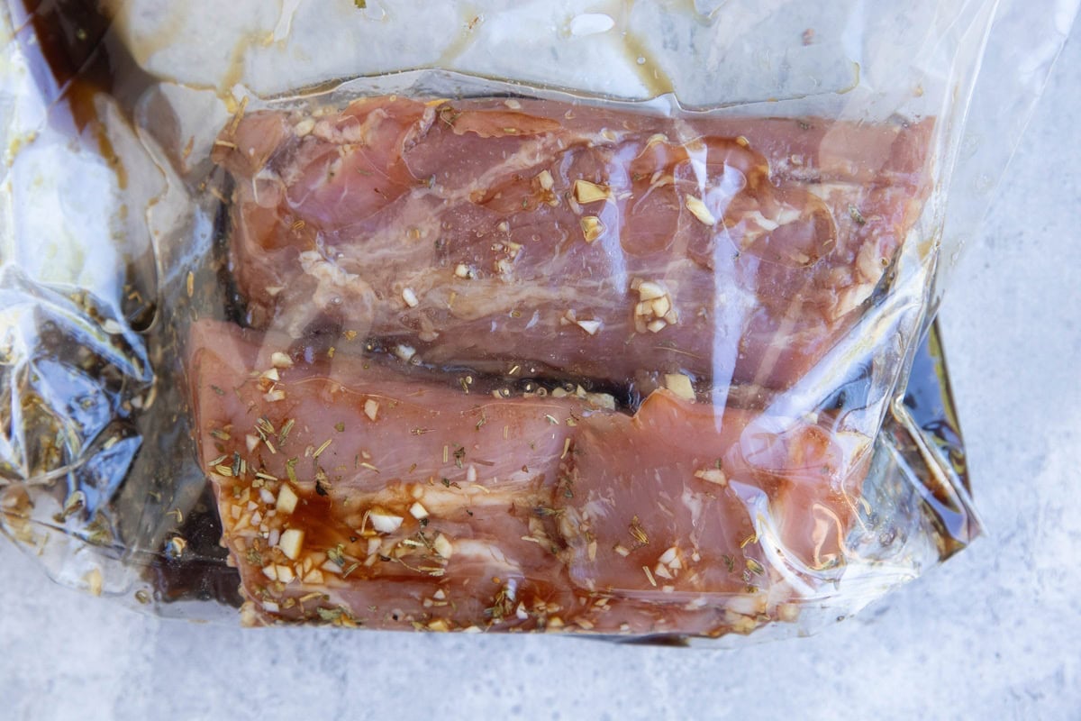 Pork tenderloin cut in half inside of a zip lock bag with pork marinade.