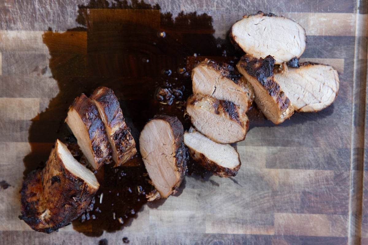 Wooden cutting board with pork tenderloin medallions cut into rounds and ready to serve.
