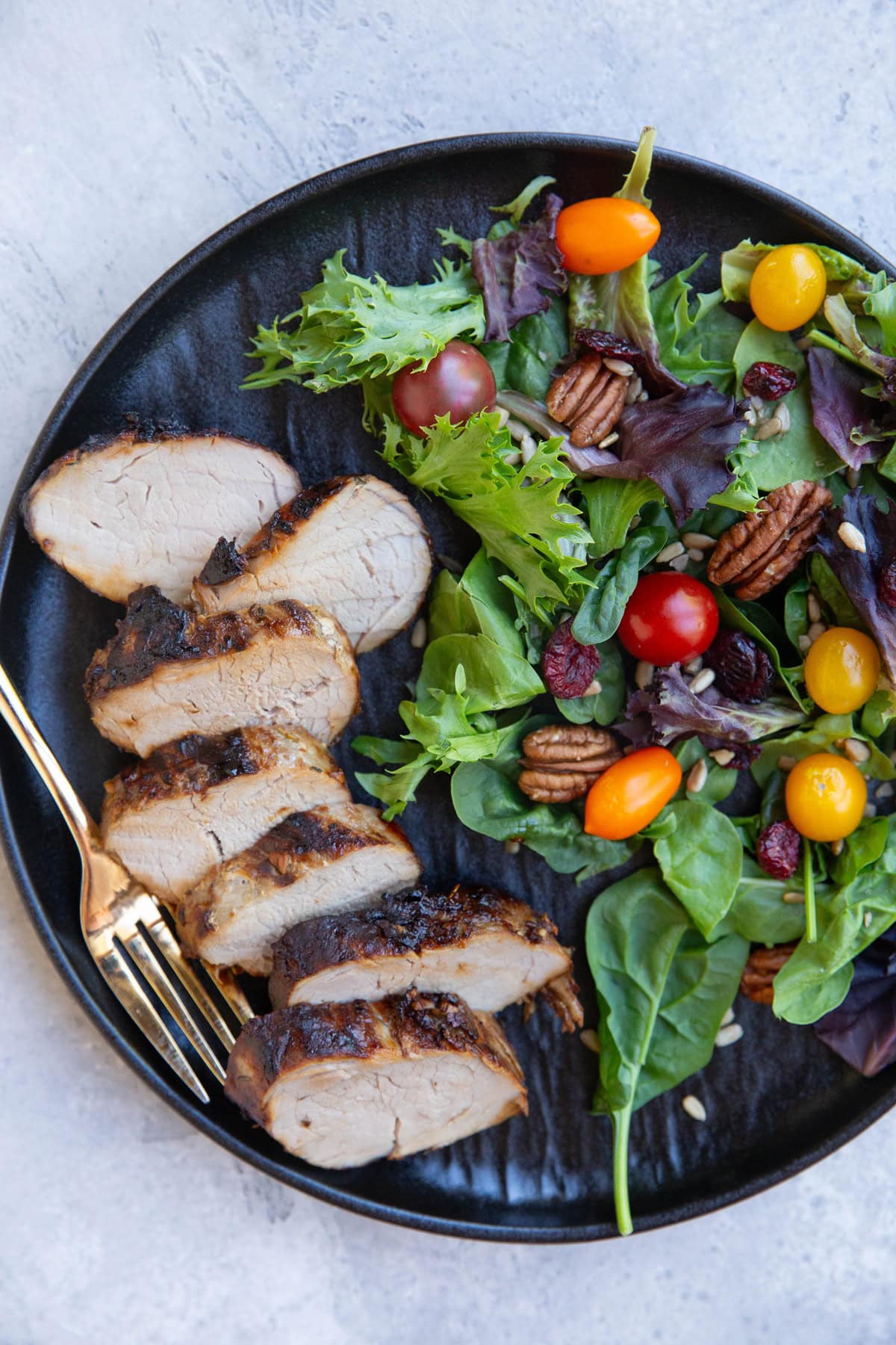 Black plate with sliced pork tenderloin and a side salad with a golden fork.