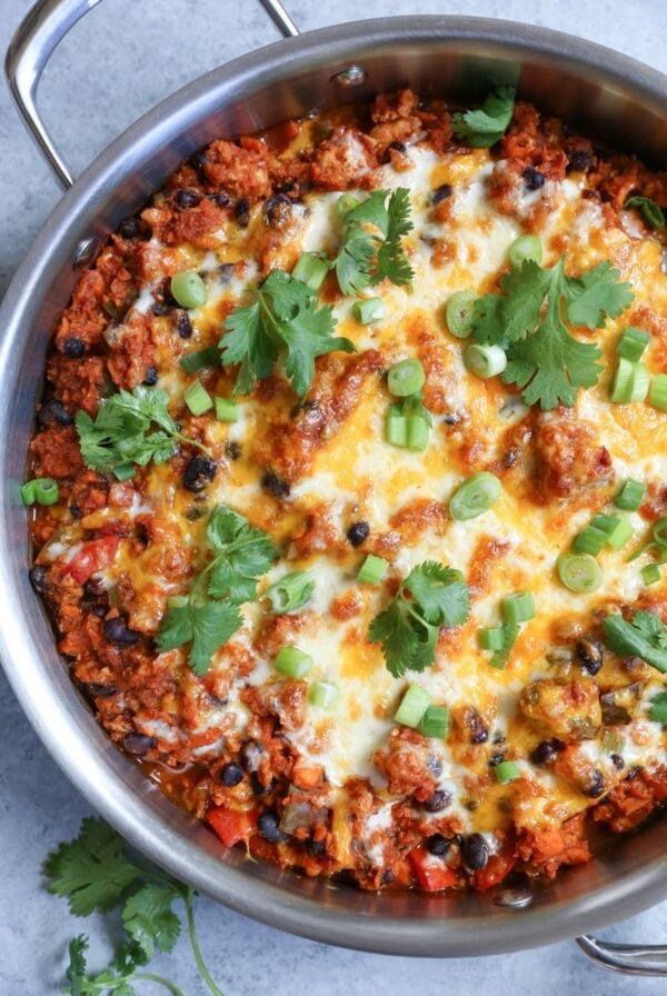 Ground turkey enchilada skillet inside of a large stainless steel skillet topped with green onions and cilantro, ready to serve.