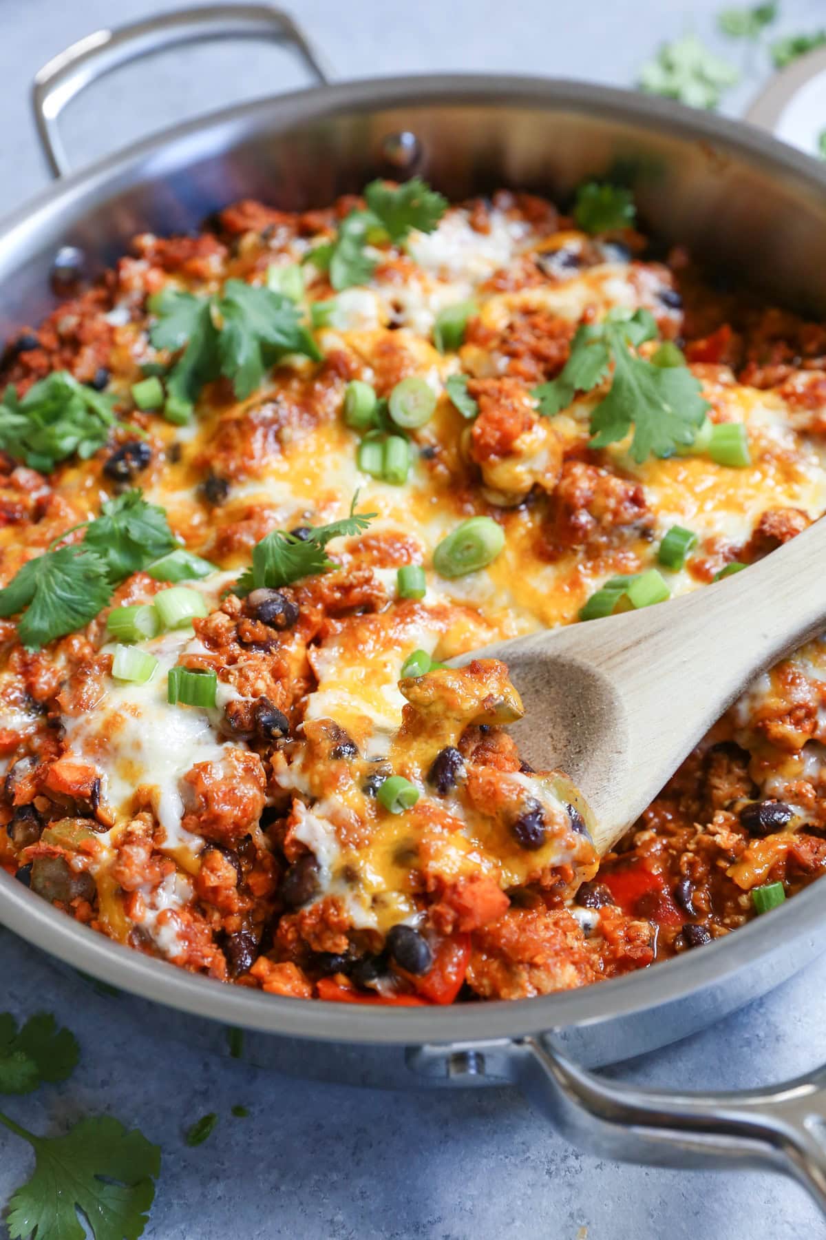 Large skillet with ground turkey, black beans, rice, and cheese and a wooden spoon scooping out a portion to serve.