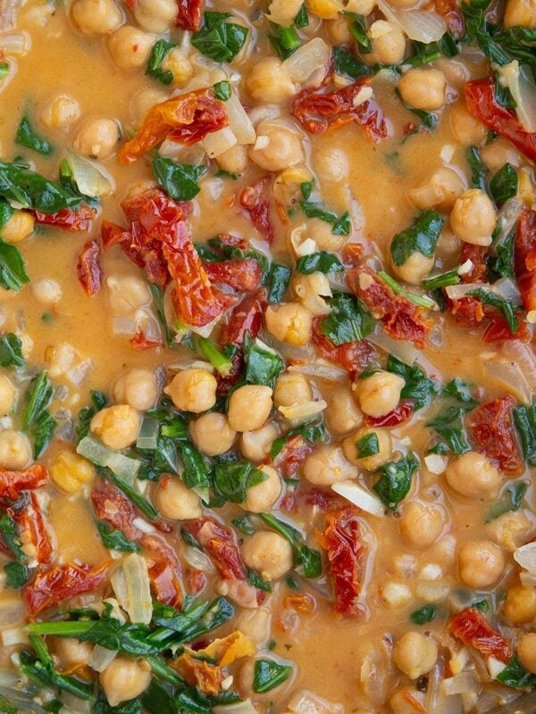 Stainless steel skillet with chickpeas in a creamy sun-dried tomato sauce with spinach.