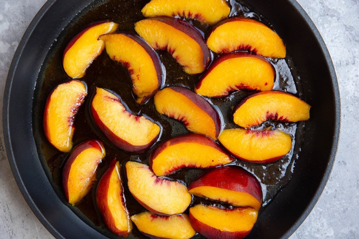 Skillet with peaches caramelizing in oil and pure maple syrup to put on top of cake.