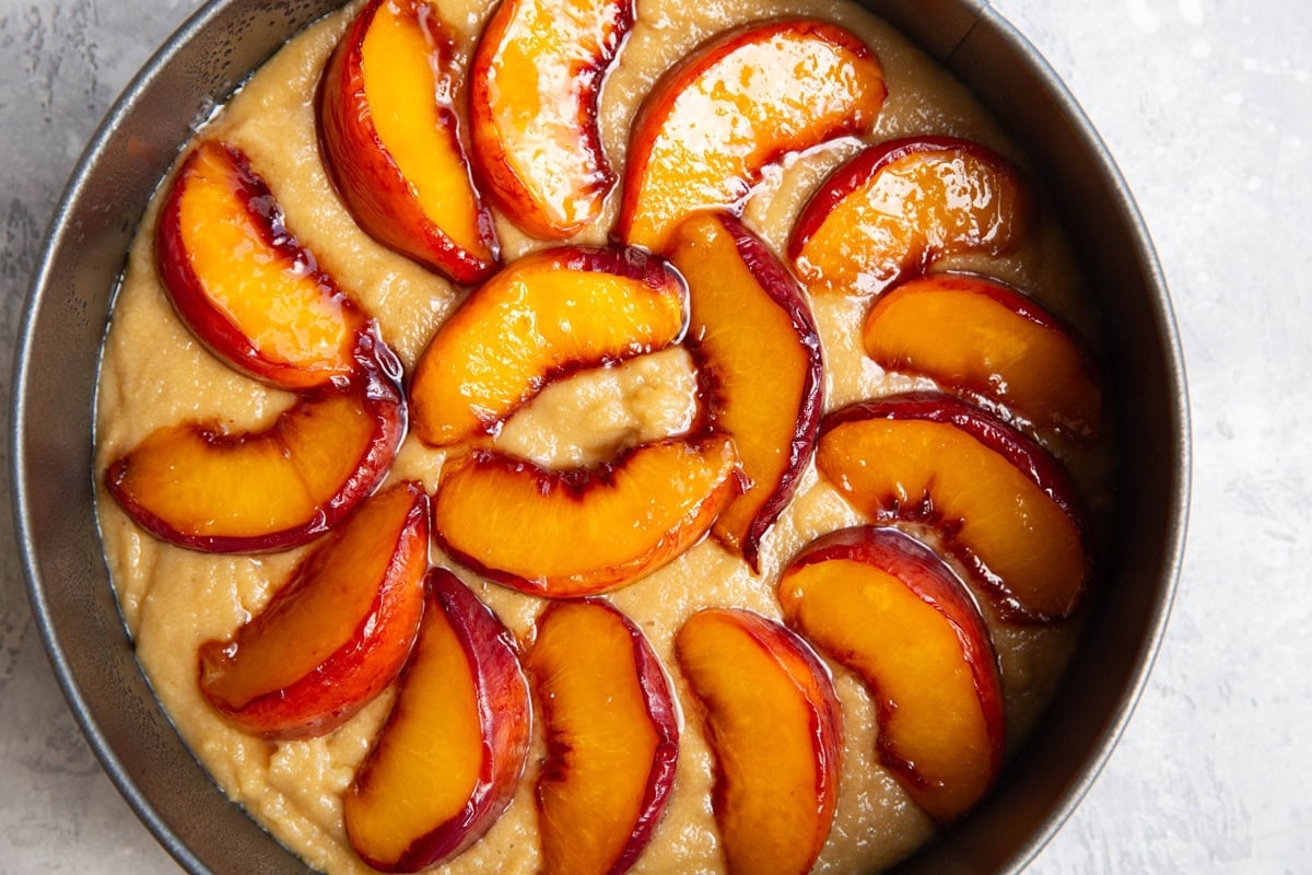 Cake batter inside of a springform cake pan with caramelized peaches on top.