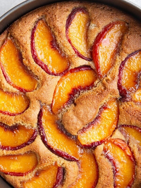 Peach cake in a cake pan fresh out of the oven with a golden brown top, ready to slice and serve.
