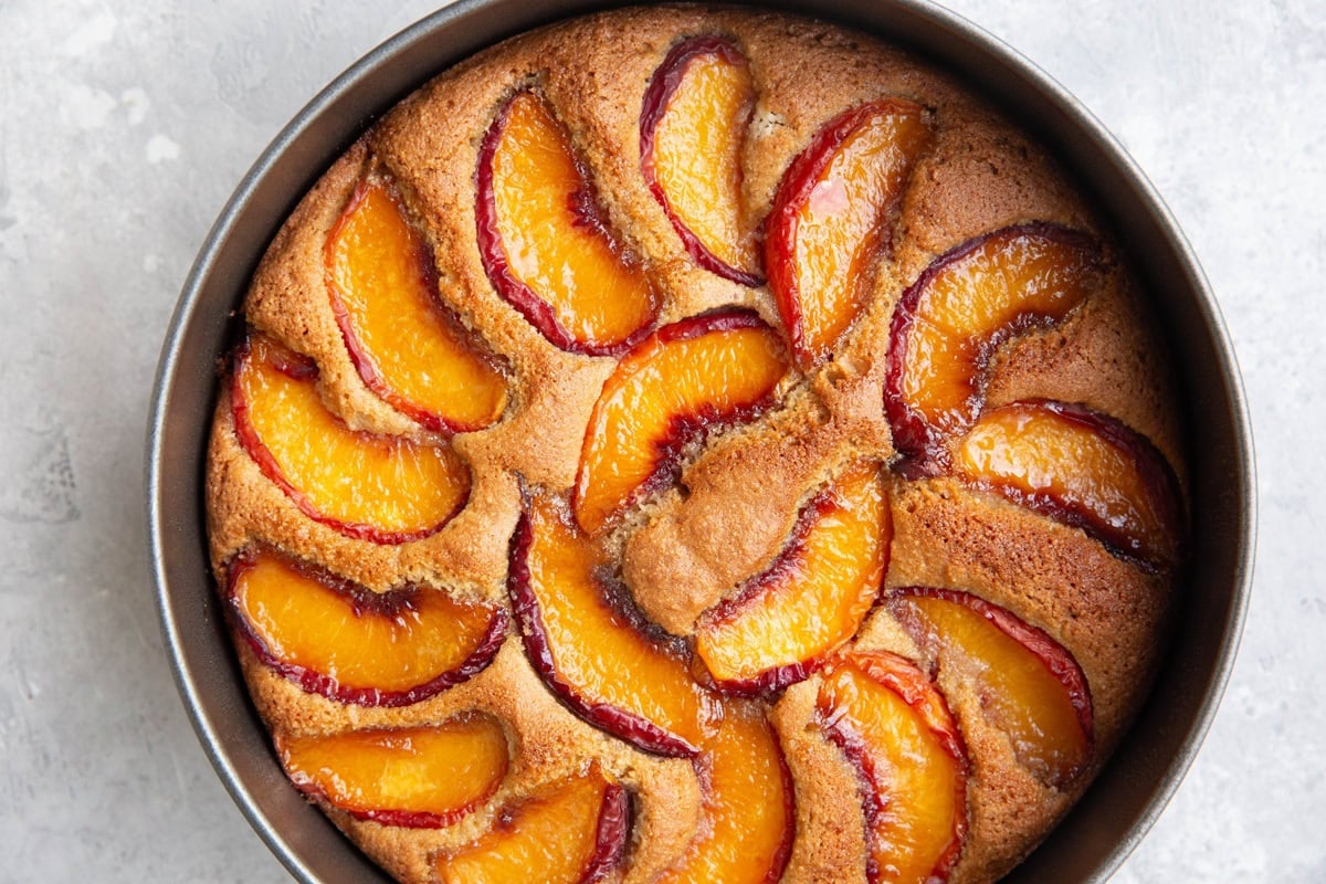 Peach cake in a cake pan fresh out of the oven with a golden brown top, ready to slice and serve.