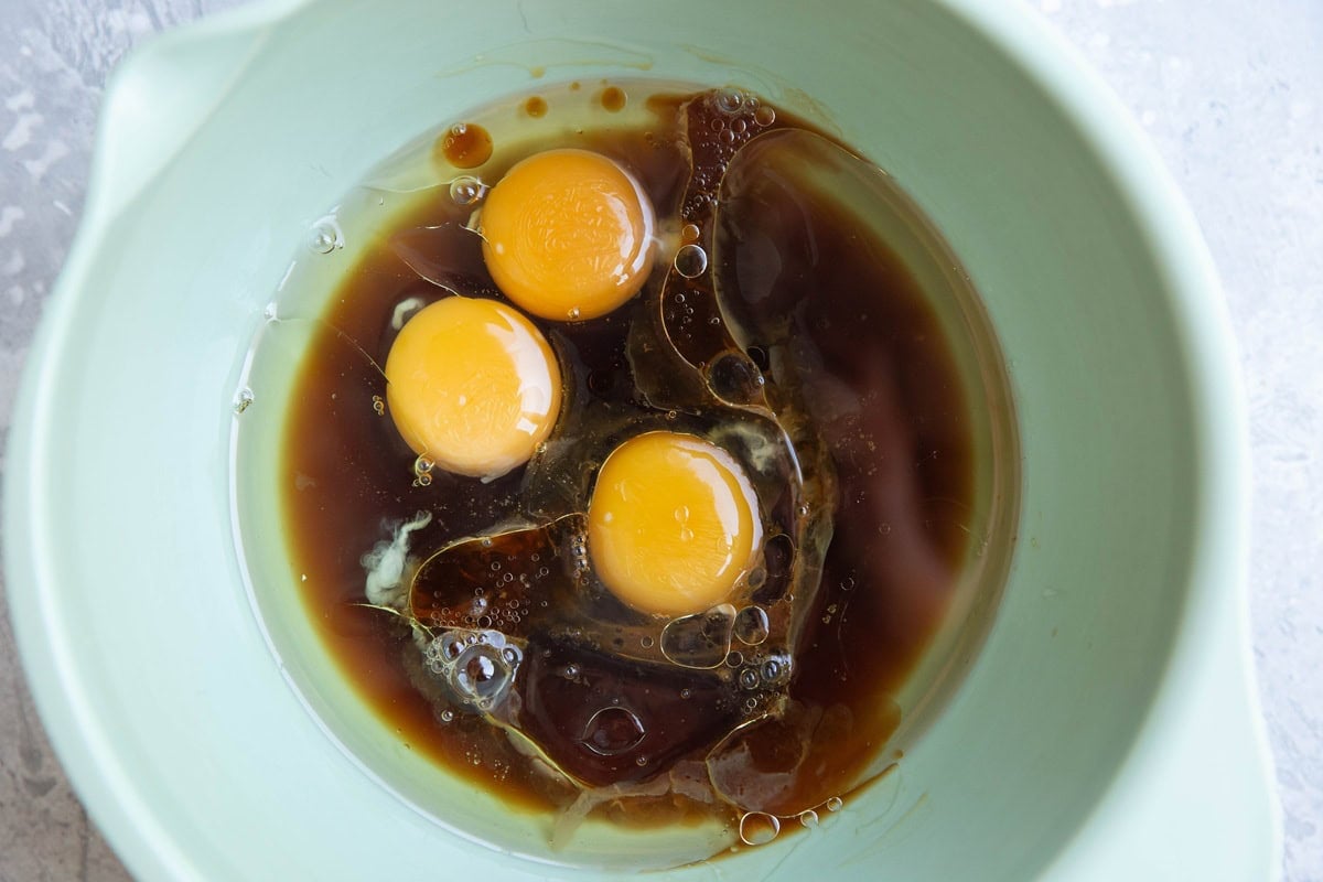 Mixing bowl with eggs, pure maple syrup, and avocado oil to make cake, ready to be mixed together.