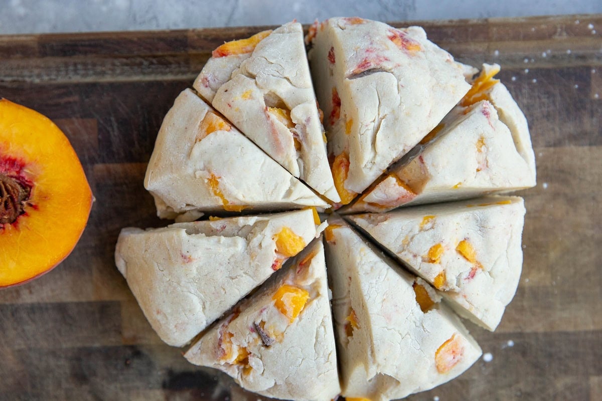 Peach scone dough on a wooden cutting board, cut into 8 triangles, ready to bake.