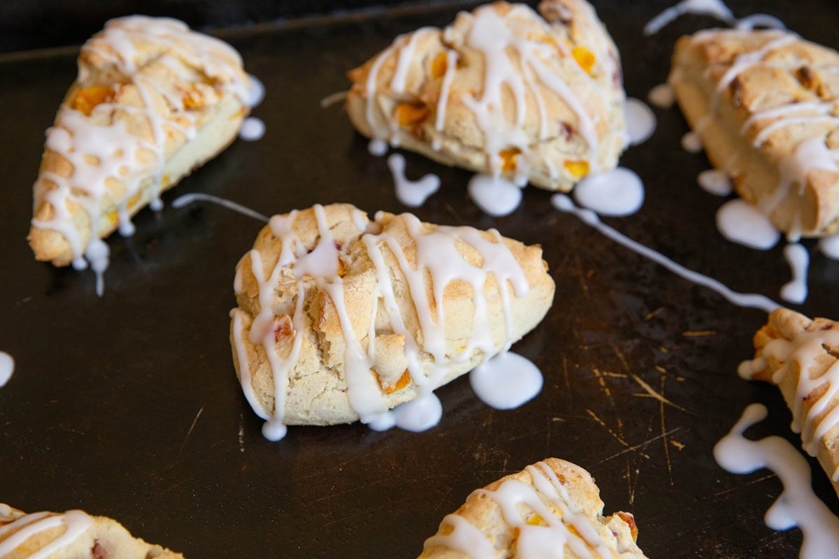 Peach scones drizzled with glaze on a baking sheet.