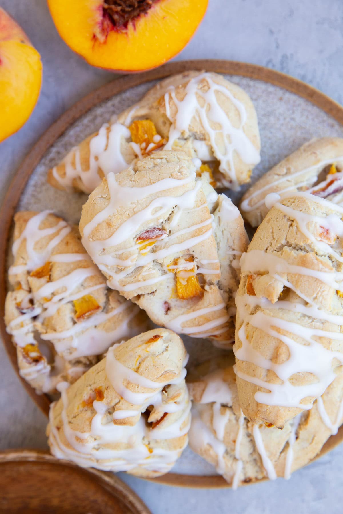 Plate full of peach scones with a peach cut in half to the side.