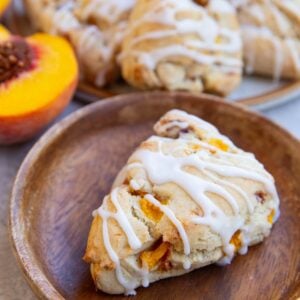 Wooden plate with a peach scone and the rest of the sconed in the background and a fresh peach.