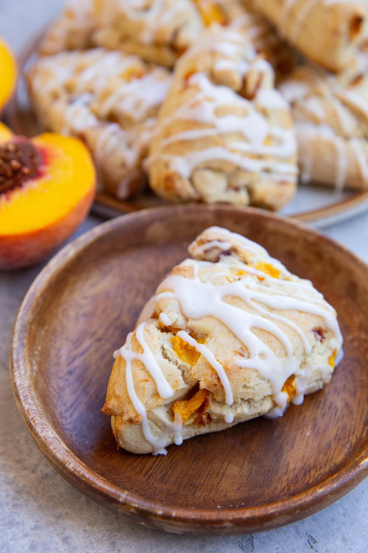 Wooden plate with a peach scone and the rest of the sconed in the background and a fresh peach.