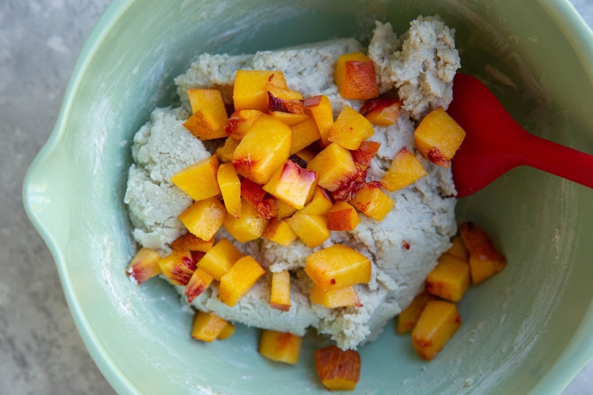 Mixing bowl full of scone dough with chopped ripe peach on top, ready to be mixed in.