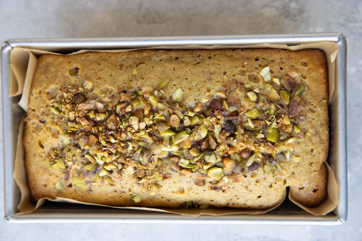Loaf pan with pistachio cake sprinkled with pistachios inside, fresh out of the oven.