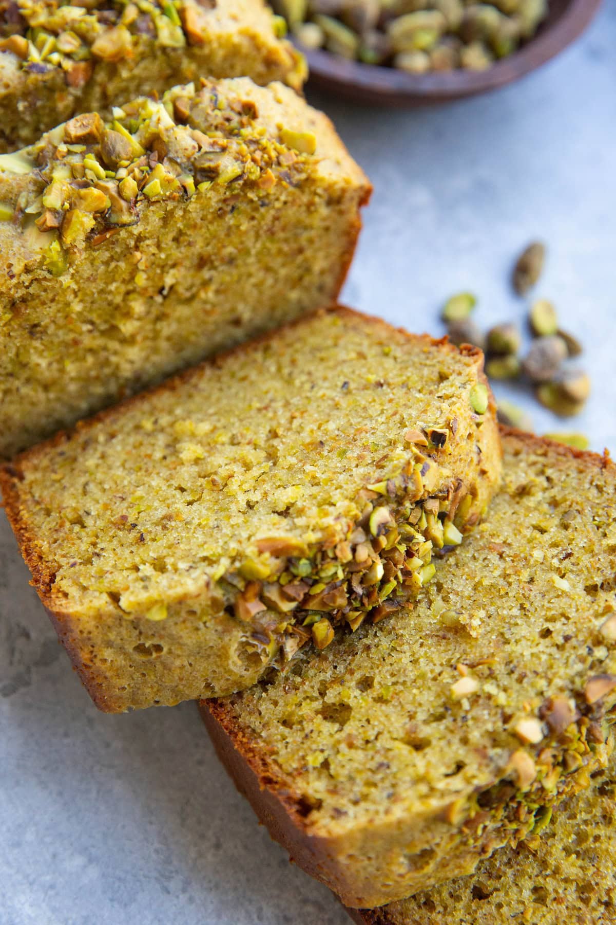 Thick slices of pistachio cake with raw pistachios in the background. The slices are in the form of a loaf.