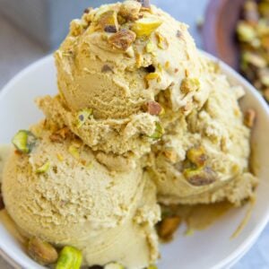 Three scoops of pistachio ice cream in a small white bowl with chopped pistachios on top. Ready to serve.