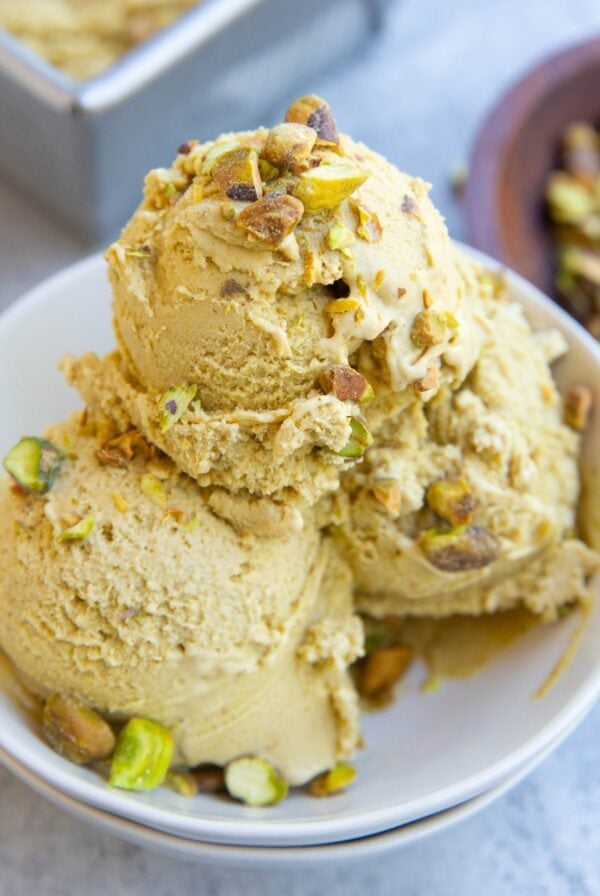 Three scoops of pistachio ice cream in a small white bowl with chopped pistachios on top. Ready to serve.