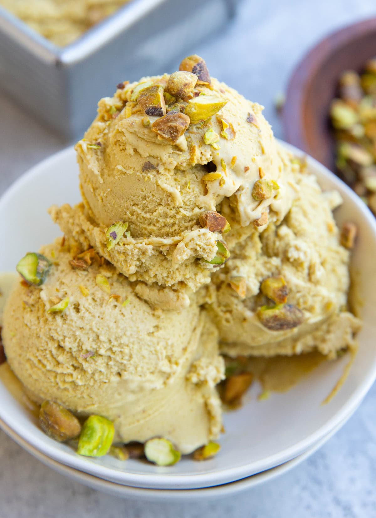 Three scoops of pistachio ice cream in a small white bowl with chopped pistachios on top. Ready to serve.