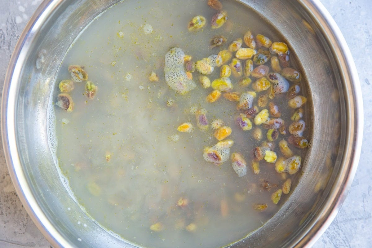 Stainless steel bowl full of raw pistachios soaking.