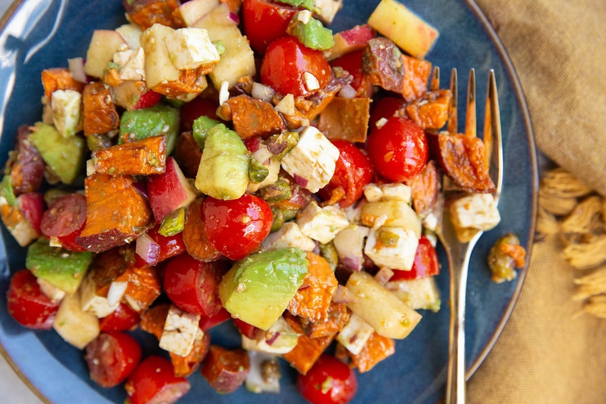 Blue plate of roasted sweet potatoes, apples, feta cheese, tomatoes, avocado and pistachios.
