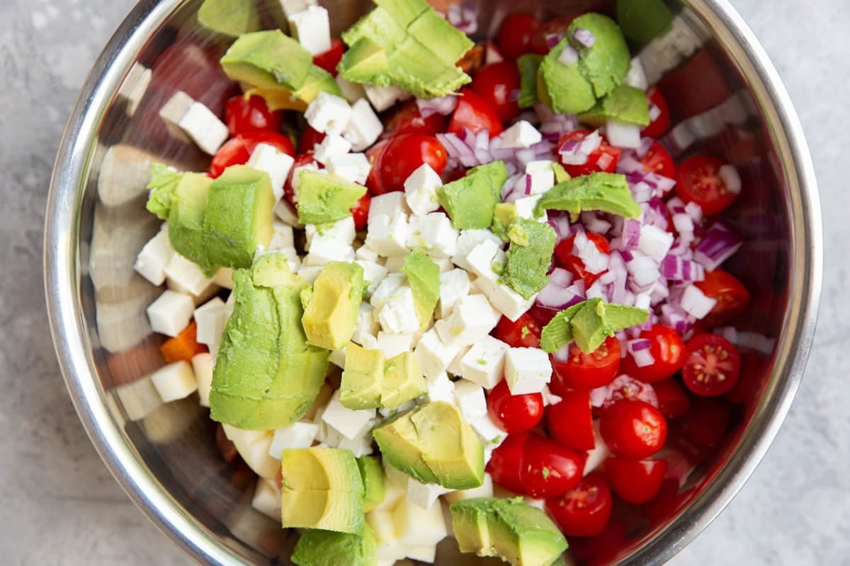 Large stainless steel bowl with roasted sweet potatoes, cherry tomatoes, avocado, feta cheese, red onion, and more.