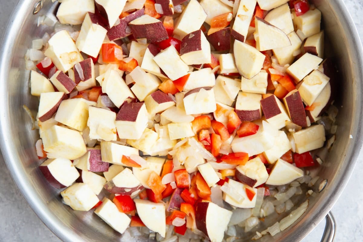 Stainless steel skillet with onion, bell pepper, and sweet potatoes cooking in the skillet.