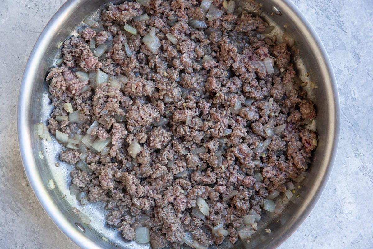 Stainless steel skillet with onions, garlic, and ground beef browning to make meat sauce.