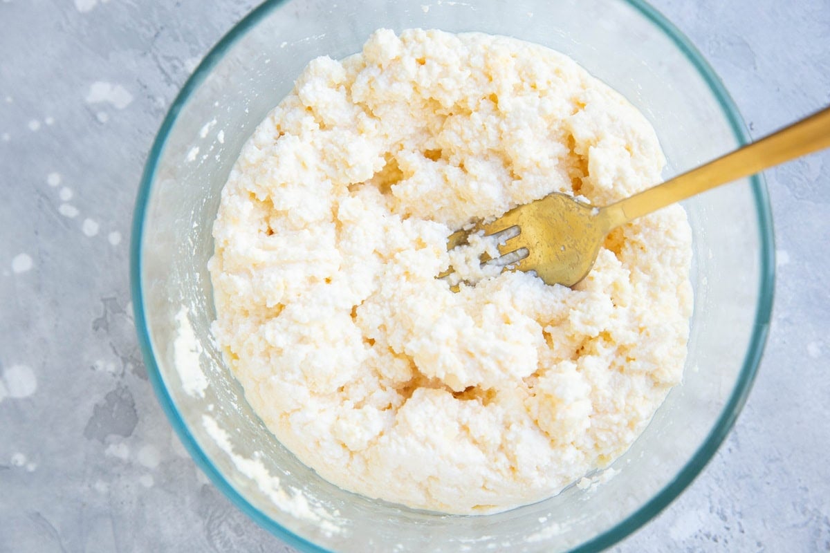 Clear glass bowl with ricotta mixture and a gold fork inside. Mixed up and ready to use.