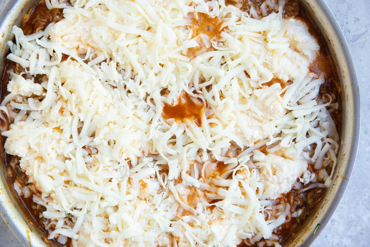 Stainless steel skillet with zucchini tomato sauce, rictotta cheese and grated mozzarella on top to make skillet lasagna.