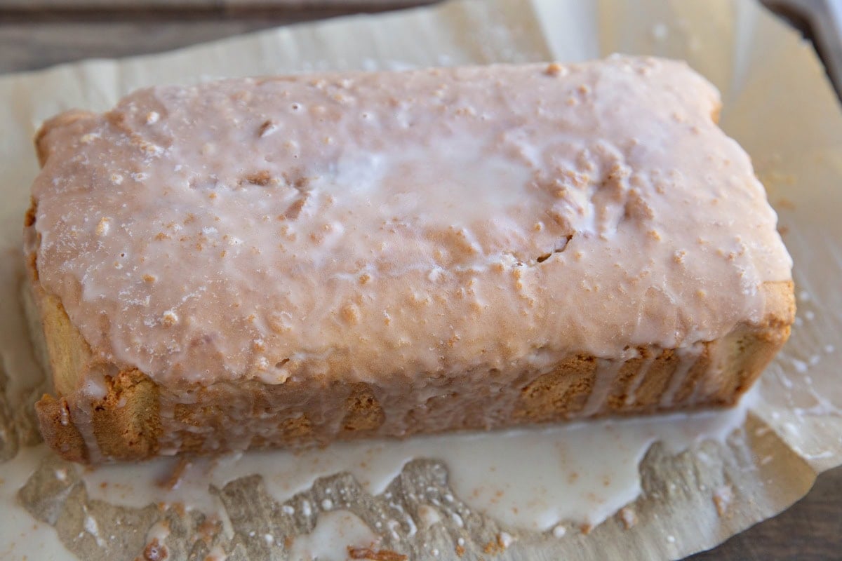 Loaf of bread sitting on parchment paper with a glaze poured over the top. Ready to cut into slices.