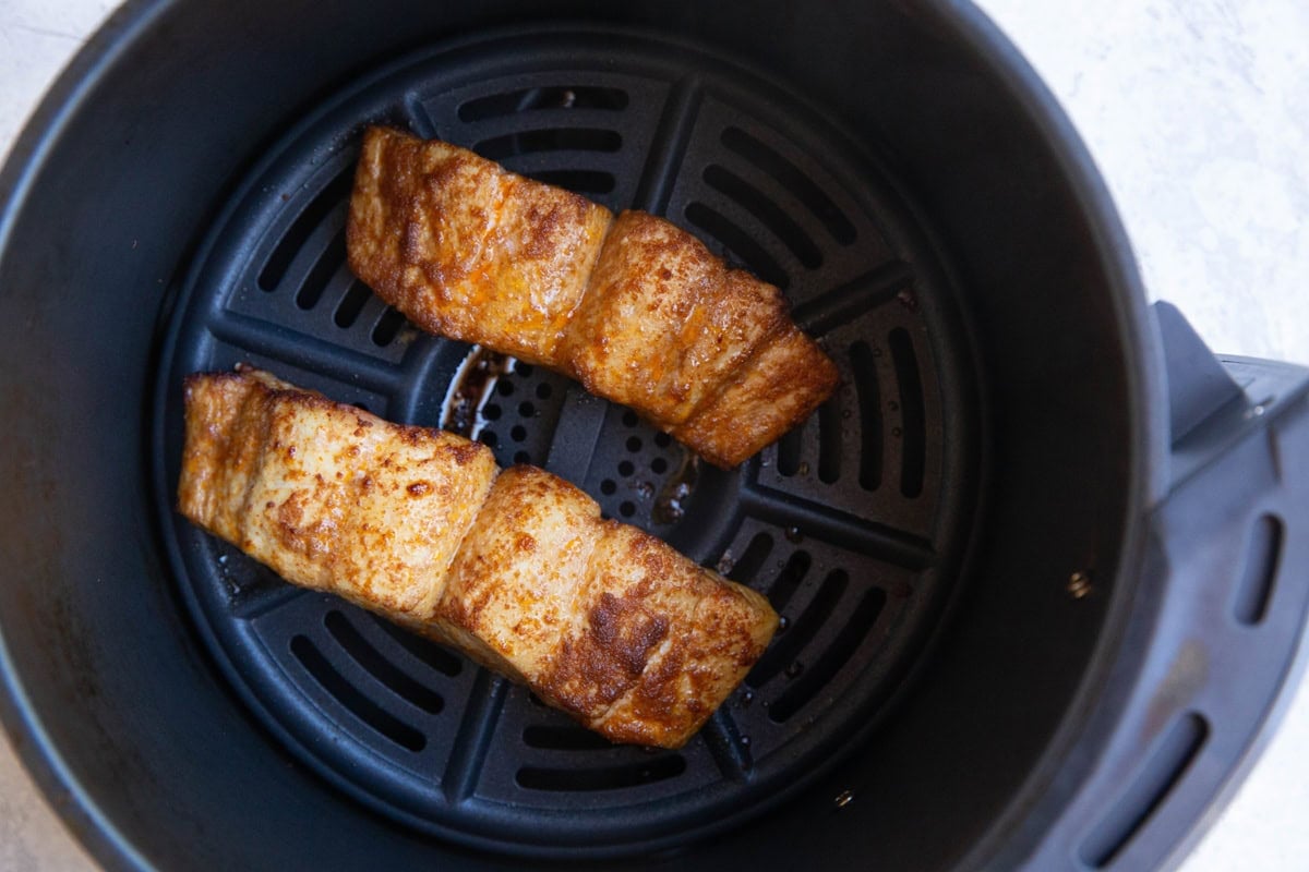 Air fryer with two cooked halibut filets inside.