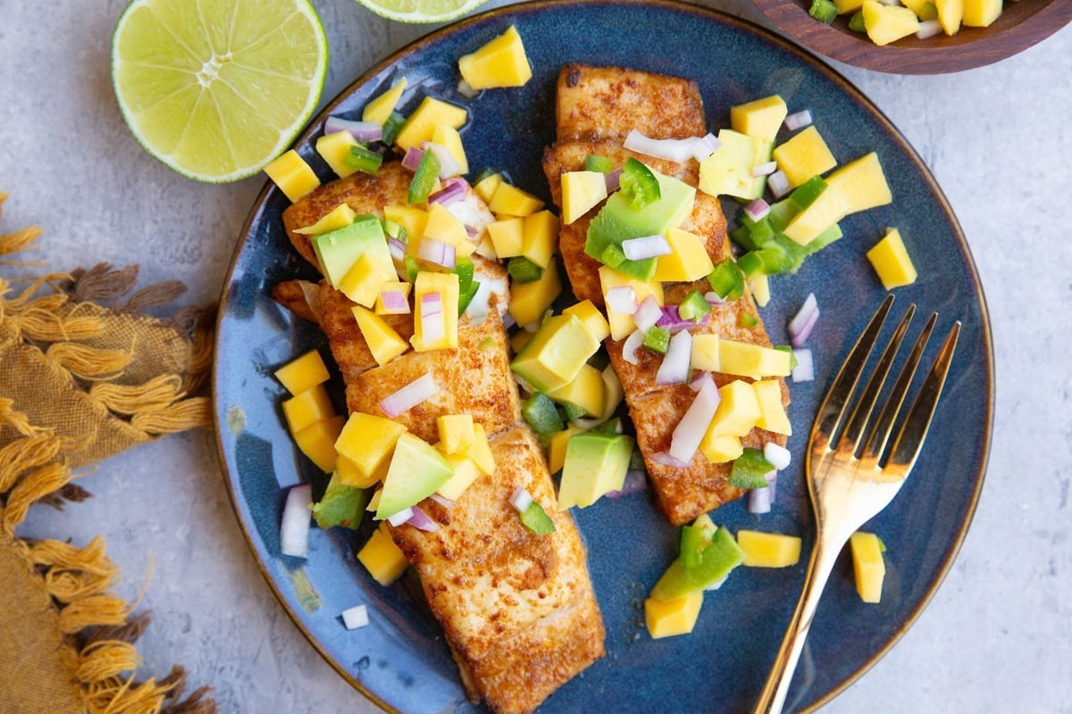 Two halibut filets on a blue plate with mango salsa on top.