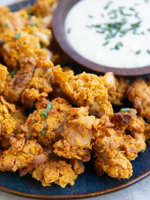 Popcorn chicken on a blue plate with a wooden bowl of ranch dressing, sprinkled with chives, ready to serve.