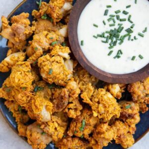Blue plate of crispy chicken pieces and a bowl full of ranch dressing sprinkled with chives, ready to serve.