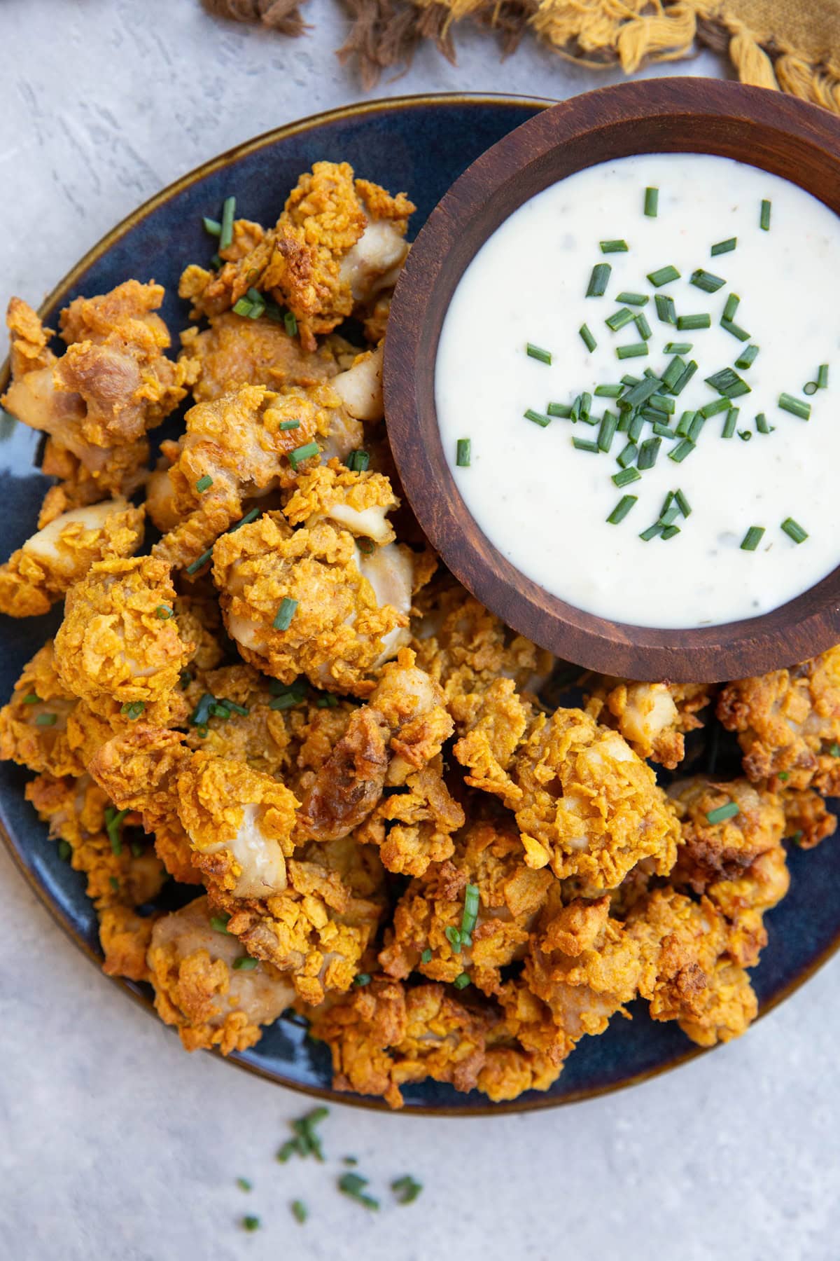 Blue plate of crispy chicken pieces and a bowl full of ranch dressing sprinkled with chives, ready to serve.