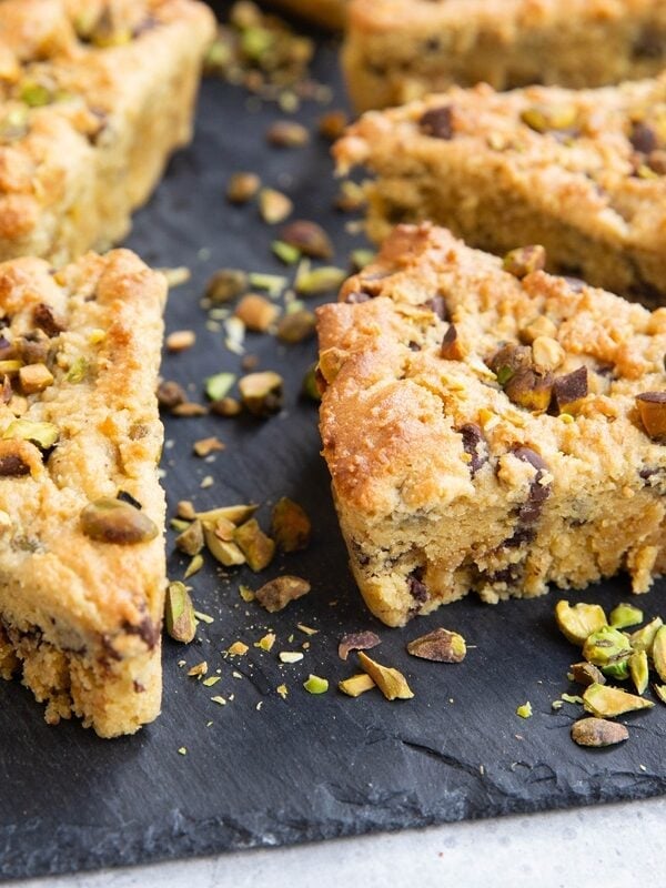 Black slate cutting board with pistachio scones with chopped pistachios all around.