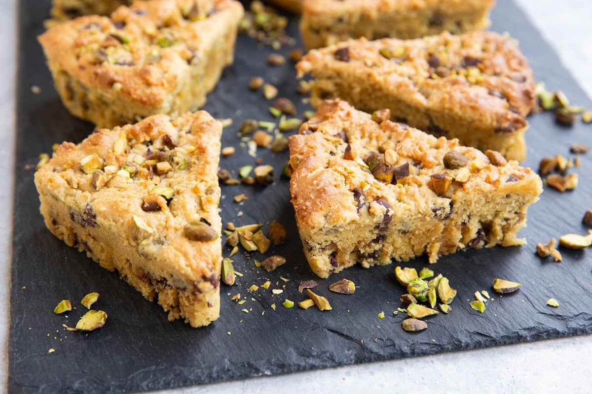 Black slate cutting board with pistachio scones with chopped pistachios all around.