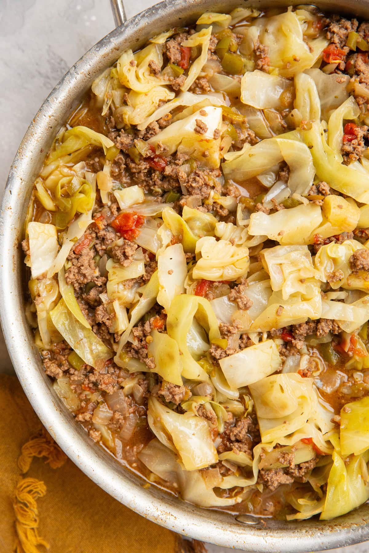 Stainless steel skillet with ground beef, cooked cabbage in a rich broth with tomatoes and peppers.