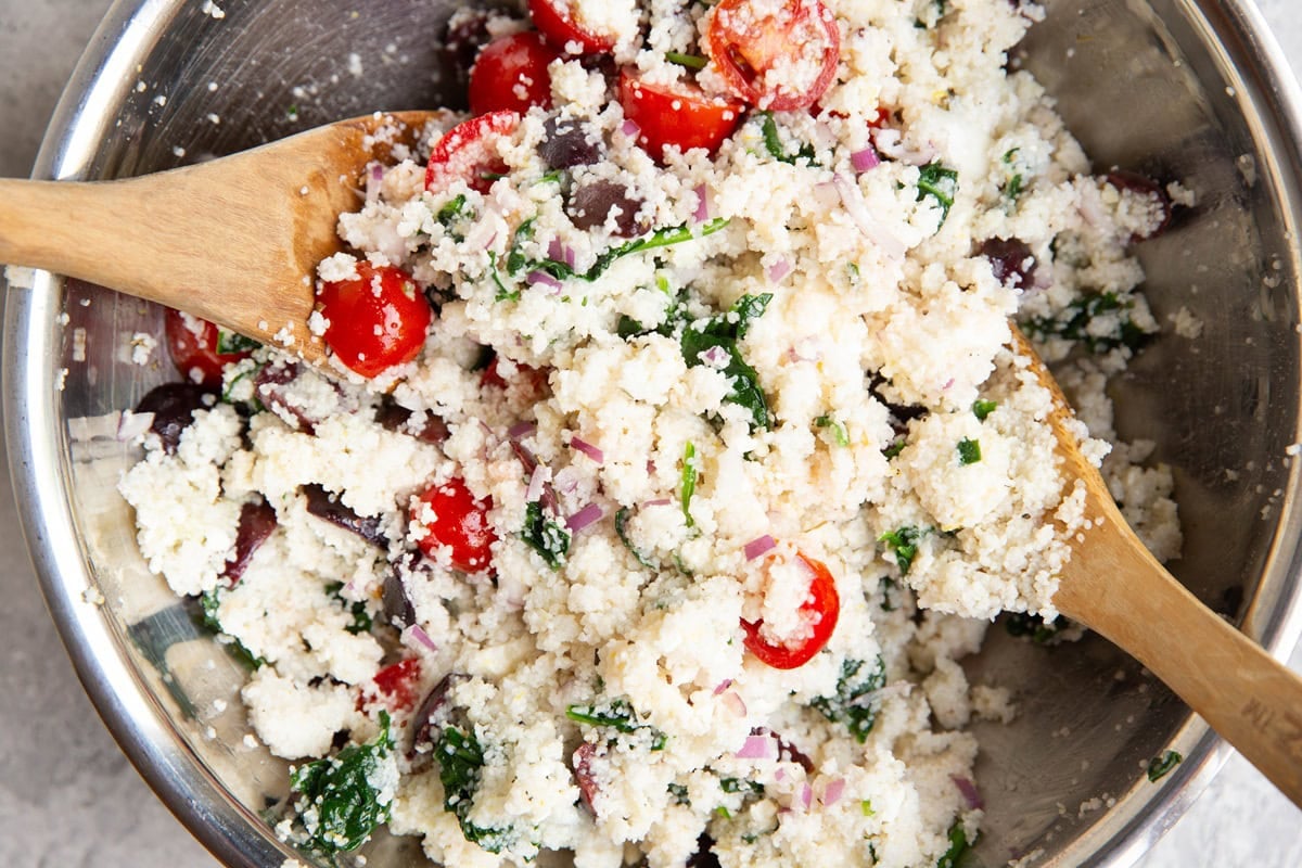 Stainless steel bowl of couscous salad with two wooden spoons that have been used to toss everything together.